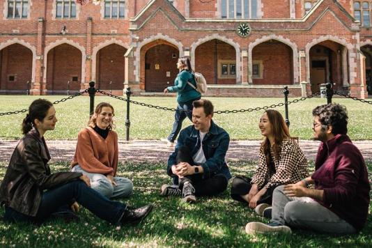 Group of five individuals sitting on the grass in the QUB Lanyon building quad area.